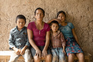 Eine Frau und drei Kinder sitzen vor einer Lehmwand. Sie blicken ernst in die Kamera.