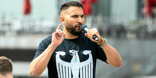 Attila Hildmann spricht in ein Mikrofon und trägt ein schwarzes T-shirt mit weiß aufgedruckten Bundesadler