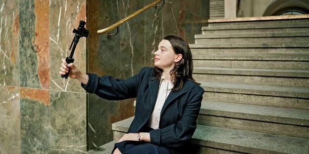 Sophie Scholl (Luna Wedler) sitzt mit Stativ und Kamera auf einer Treppe