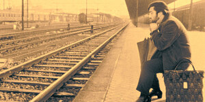 Lucio Dalla sitzt nachdenklich an einem leeren Bahngleis, das Foto ist sepiafarben.