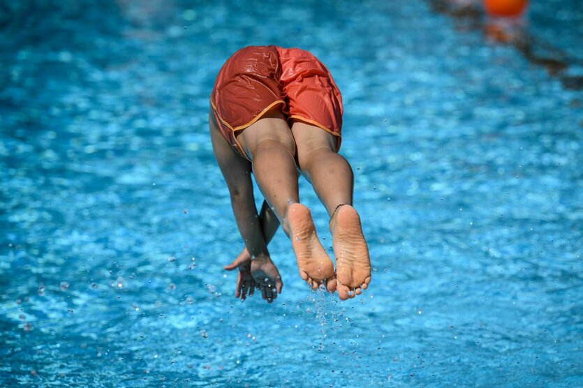 Ein Junge springt im Sommerbad Neukölln ins Schwimmbecken.