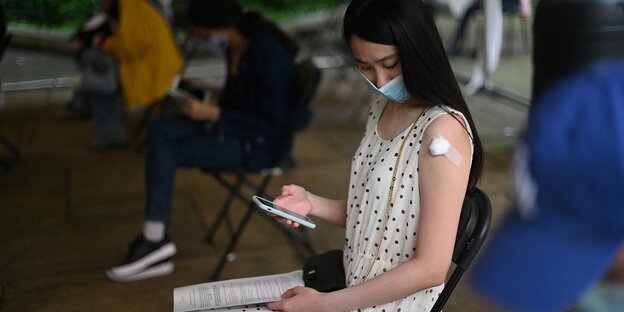 Eine Studentin mit Pflaster auf dem Arm wartet im Impfzentrum