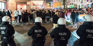 Behelmte Polzist:innen stehen in einer Reihe feiernden Menschen gegenüber