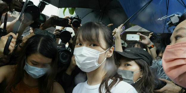Aktivistin Agnes Chow mit Maske umringt von anderen Menschen mit Maske blickt in die Kamera
