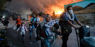 ARCHIV - 09.09.2020, Griechenland, Lesbos: Migranten fliehen vor einem erneuten Feuers mit ihren Habseligkeiten aus dem Flüchtlingslager Moria, nachdem zuvor bereits mehrere Feuer das Lager nahezu vollständig zerstört haben.