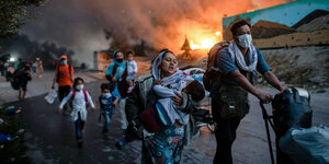 ARCHIV - 09.09.2020, Griechenland, Lesbos: Migranten fliehen vor einem erneuten Feuers mit ihren Habseligkeiten aus dem Flüchtlingslager Moria, nachdem zuvor bereits mehrere Feuer das Lager nahezu vollständig zerstört haben.