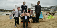 Großbritannien, St Ives: Einige Aktivisten der Extinction Rebellion Bewegung tragen am Strand Pappmasken mit Fotos, die die Staats- und Regierungschefs, (v.l) den französischen Präsident Emmanuel Macron, den britischen Premierminister Boris Johnson, US-Pr