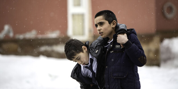 Ein etwa 12-jähriger Junge stützt einen anderen Jungen beim Gehen durch den Schnee.