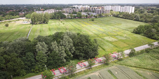 Lufbild mit einer Straße, auf der Menschen mit roten Schirmen einen Schriftzug formen, im Hintergrund eine Hochhaussiedlung