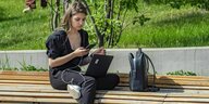 Eine Frau sitzt mit Rechner uns Smartphone auf einer Bank