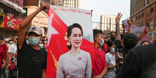 Bei einer Demonstration halten Männer ein Plakat von Aung San Suu Kyi in der Hand
