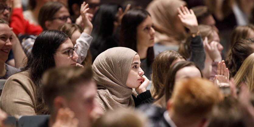 Eine junge Frau mit Kopftuch sitzt inmitten anderer junger menschen in eine Hörsaal