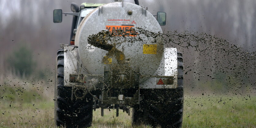 Ein Traktor mit Anhänger bringt Gülle auf einem Feld aus.