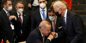 Der türkische Präsident Erdogan begrüßt im Sitzen per Handschlag den vor ihm stehenden US-Präsidenten Biden
