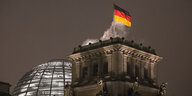 Das Reichstagsgebäude bei Nacht. Auf dem Dach vor der Kuppel eine Deutschlandfahne im Wind.