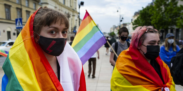 Zwei maskierte Frauen mit Regenbogenfahnen bei einer LGBTQ Demonstration