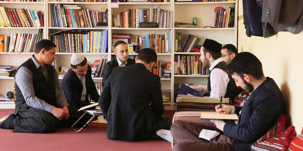 Männer sitzen vor einem Bücherregal im Kreis auf dem Boden