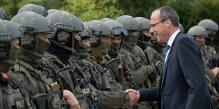 Ein mann im anzug schüttelt die Hand von schwer gepanzerten Polizisten und lacht