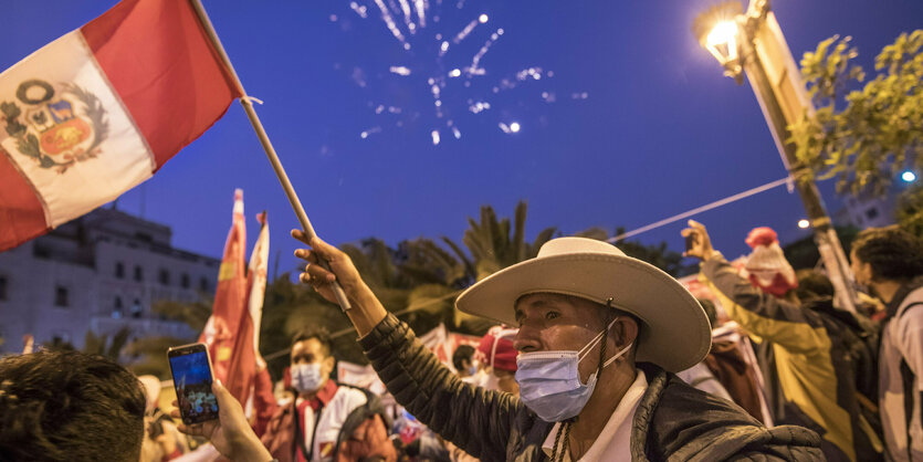 Menschen mit Fahnen stehen auf der Straße, im Abendhimmel ist Feuerwerk zu sehen