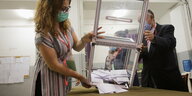 MitarbeiterInnen in einem Wahlbüro entleeren eine Box mit sehr wenigen Stimmzetteln