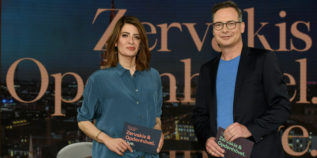 Die Moderatorin Linda Zervakis und der Moderator Matthias Opdenhövel stehen in dem Studio, in dem sie das neue ProSieben-Journal «Zervakis & Opdenhövel. Live» ab Herbst 2021 moderieren. Sie halten Karten in der Hand und stehen vor einer Werbewand.