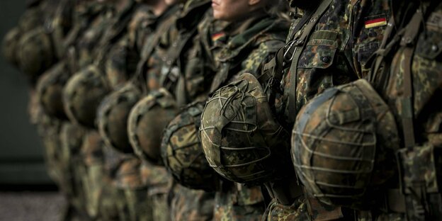 Eine Gruppe von Soldaten steht in einer Reihe, die Helme vor ihrer Brust