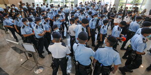 Polizisten mit Gesichtsmasken blauen Hemden und Mützen versammeln sich in einem Gebäude