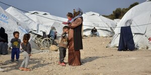 Eine Frau steht mit einem Baby im Arm und drei kleinen Kindern in einem Flüchtlingslage