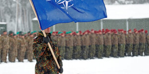 Ein deutscher Soldat mit Nato Flagge steht vor aufgereihten Bundeswehrsoldaten im Schneegestöber