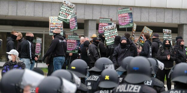 In schwarz gekleidete Demonstrierende mit Schildern und Polizisten mit Schutzhelmen