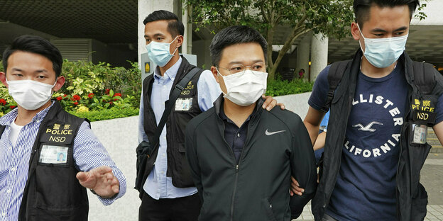 Der Chefredakteur der Zeitung Apple Daily wird von Polizisten abgeführt - alle tragen Mund-Nasenschutz