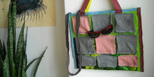 Eine Tasche, verziert mit Filzquadraten, hängt an einer Wand