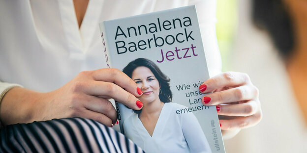 Annalena Baerbock hält ihr Buch ihrem Portait auf dem Cover und dem Titel „Jetzt. Wie wir unser Land erneuern“
