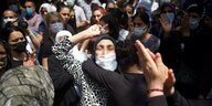 Eine Frau mit Kopftuch und Gesichtsmaske in Menschenmenge weint und schreit