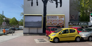 Parkplatz in Berlin mit Plakatwand, auf der eine afrikanische Landschaft abgebildet ist