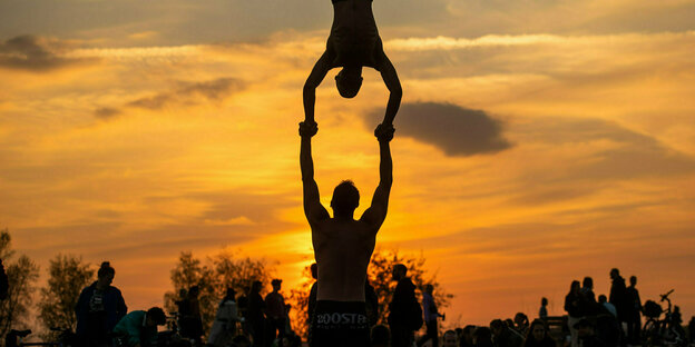 Zwei Männer machen auf dem Tempelhofer Feld während des Sonnenuntergangs akrobatische Übungen