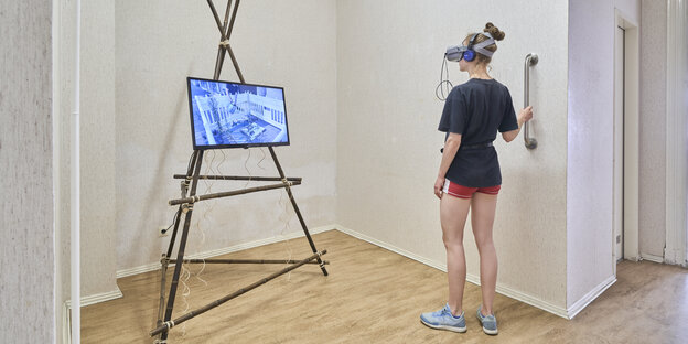 Eine Frau mit VR-Brille neben ihr ein Bildschirm
