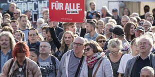 Auf einer Wahlveranstaltung hält eine Frau ein Schild hoch auf dem FÜR ALLE, Die Linke steht