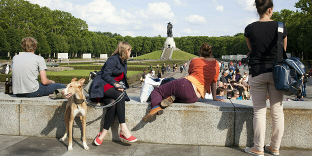 Frauen sitzen mit einem hund auf einer Mauer vor dem sowjetischen Denkmal im Treptower Park