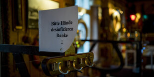 Ein Schild mit der Aufschrift "Bitte Hände desinfizieren" in einer schummerigen Kneipe