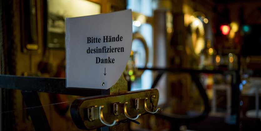 Ein Schild mit der Aufschrift "Bitte Hände desinfizieren" in einer schummerigen Kneipe