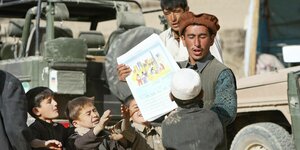 Ein afghanischer Mann verteilt Zeitungen an Kinder im Auftrag der Bundeswehr