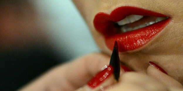 Eine Frau schminkt sich die Lippen strahlend rot