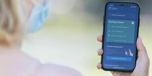Eine Frau blickt auf ihr Handy, auf dem die Corona-Warn App geöffnet ist