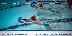 Zwei Kinder schwimmen in einem Schwimmbad mit Schwimmbrettern