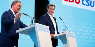 Armin Laschet und Markus Söder stehen an zwei Rednerpulten. Hinter ihnen eine Wand voller Logos von CDU und CSU. Die beiden sind ältere Männer. Laschet ist kleiner als Söder