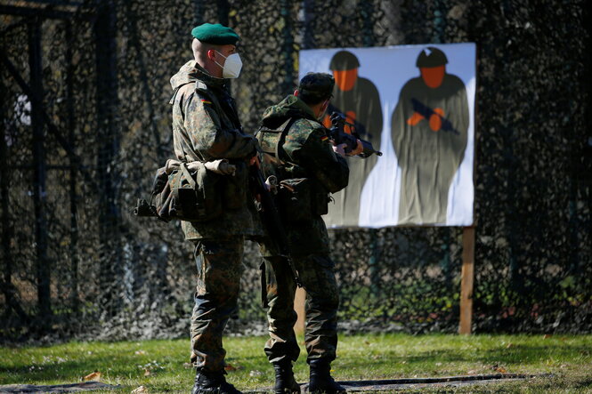 Ein Ausbilder der Bundeswehr unterrichtet einen Freiwilligen im Schießen. Der Freiwillige zielt auf die Darstellung von zwei bewaffneten Soldaten.