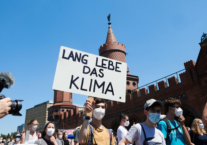 Demonstration vor der Brücke an der Wahrschauer Straße in Berlin. die menschen tragen Masken und halten Schilder in die Luft. Auf einem steht: "Lang lebe das Klima"