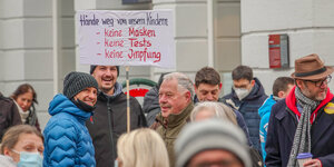 Eine Menschenansammlung, in deren mitte fünf Männer stehen. Einer von ihnen hält ein Schild mit der Aufschrift: "Hände weg von unsern KIndern - Keine Masken - Keine Tests _ Keine Impfung"