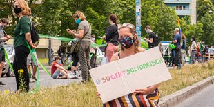 Frau hockt mit einem Schild "sogehtsolidarisch" auf dem Bordstein